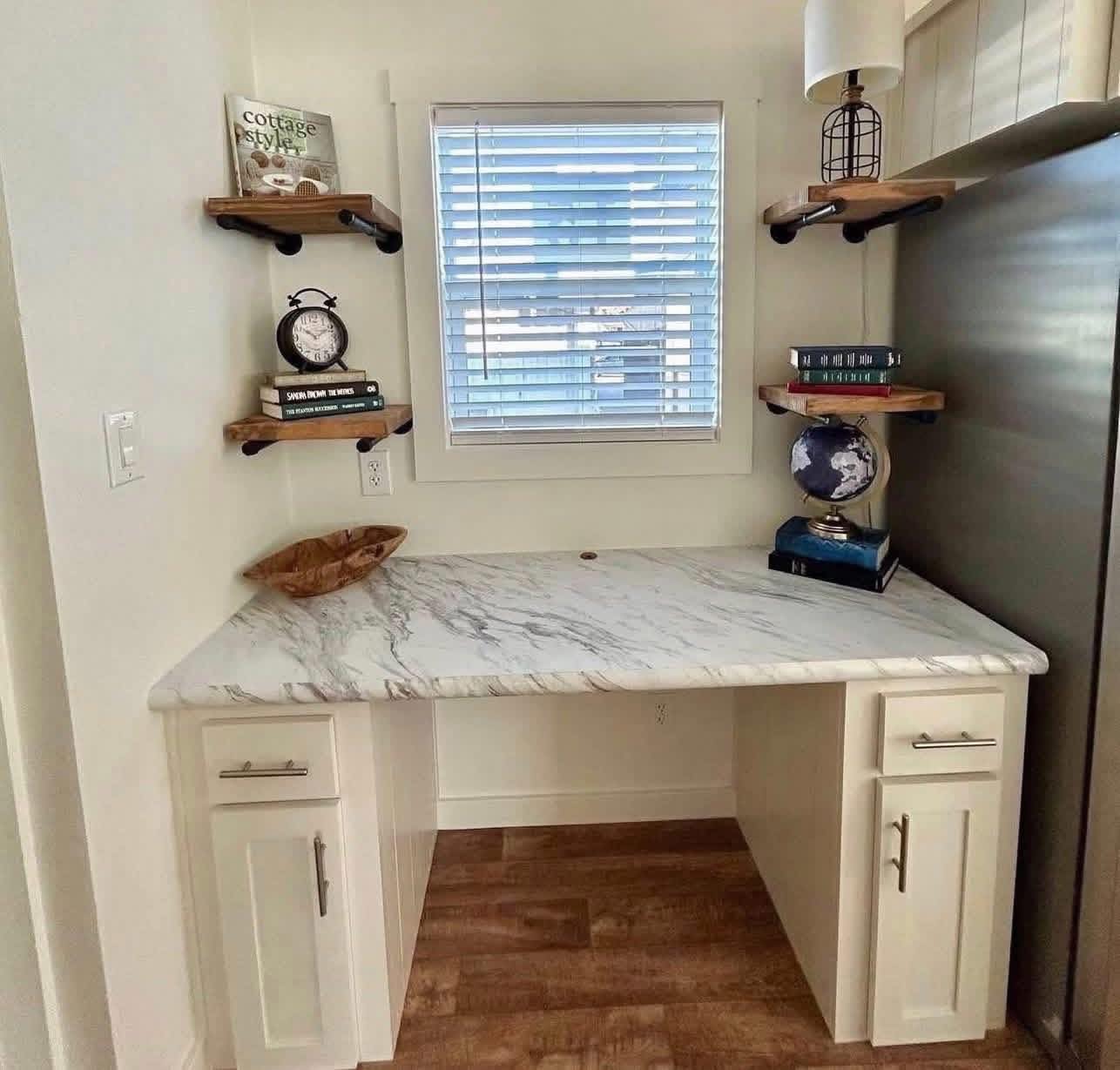 Cozy study nook with a marble desk, wooden shelves holding books and a globe, under a window with blinds. Warm, organized ambiance.