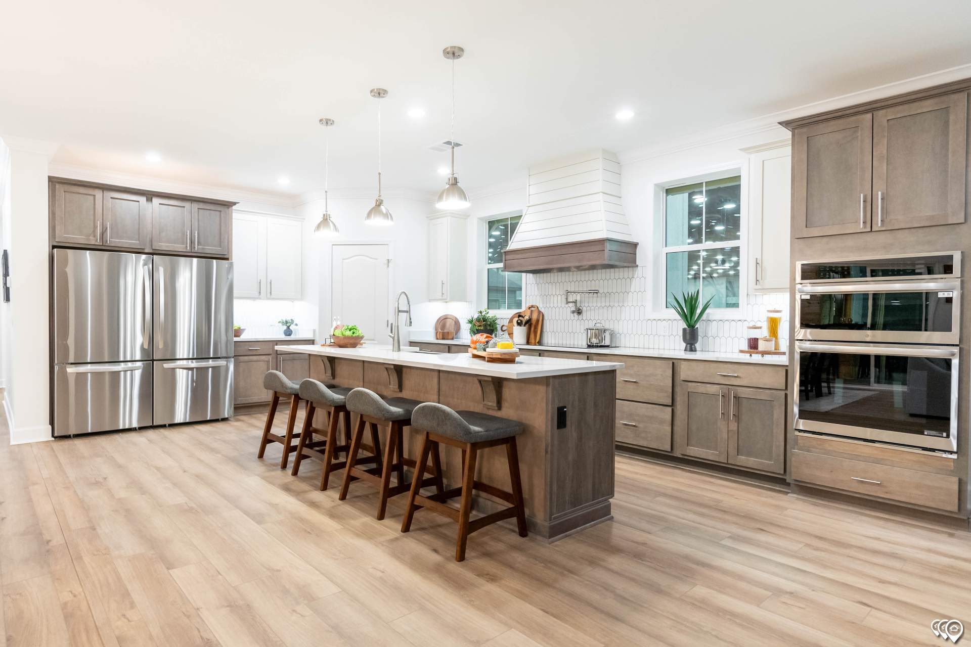 Modern kitchen featuring stainless steel appliances, a spacious island with four stools, pendant lighting, wood cabinets, and hardwood floors.