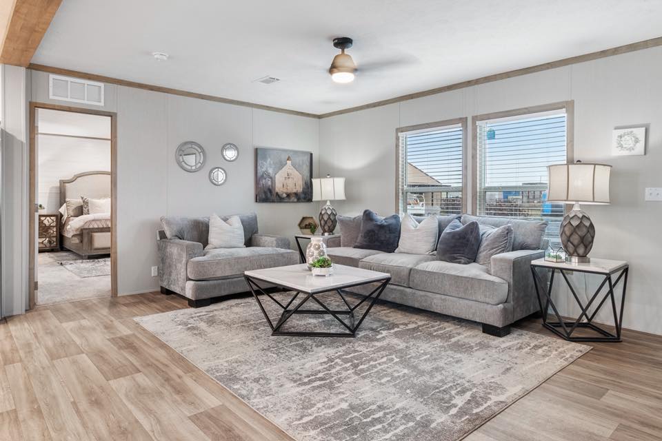 A cozy living room with gray sofas, a patterned rug, and a geometric coffee table. Soft lighting from table lamps creates a warm, inviting atmosphere.