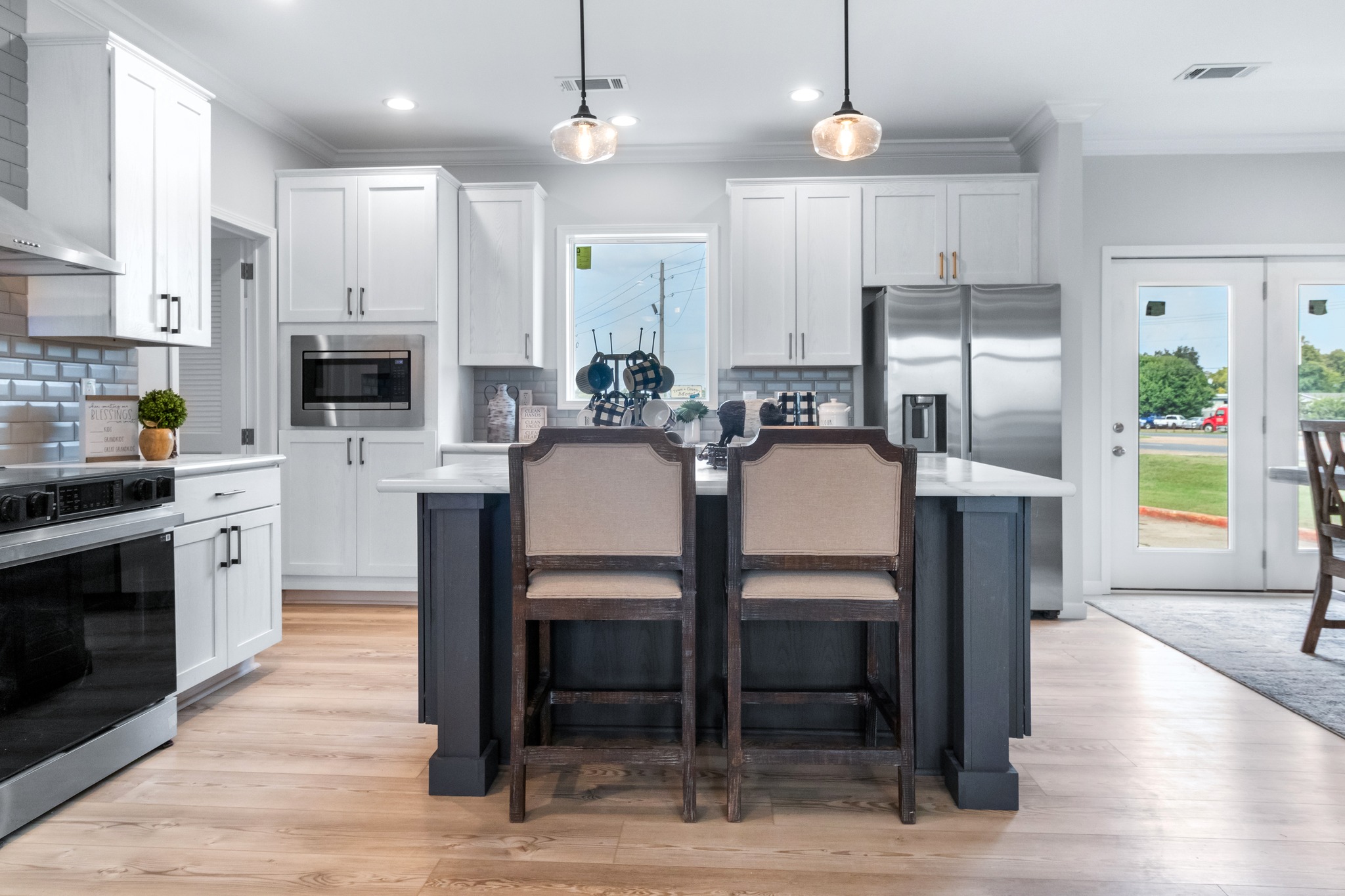 Modern kitchen with white cabinets, stainless steel appliances, and a central island with two chairs. Pendant lights create a warm ambiance.