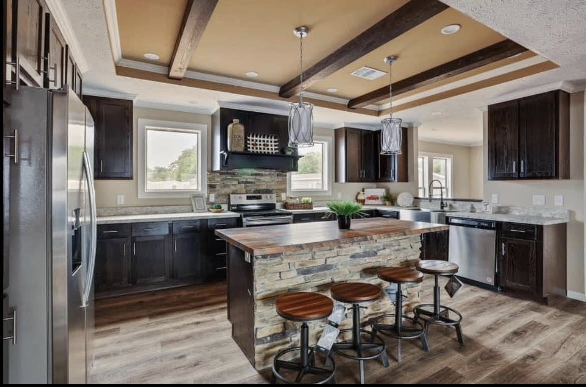 Modern kitchen with wooden beams, stone-accented island, and four stools. Dark cabinets, stainless steel appliances, and pendant lights create a warm, inviting atmosphere.