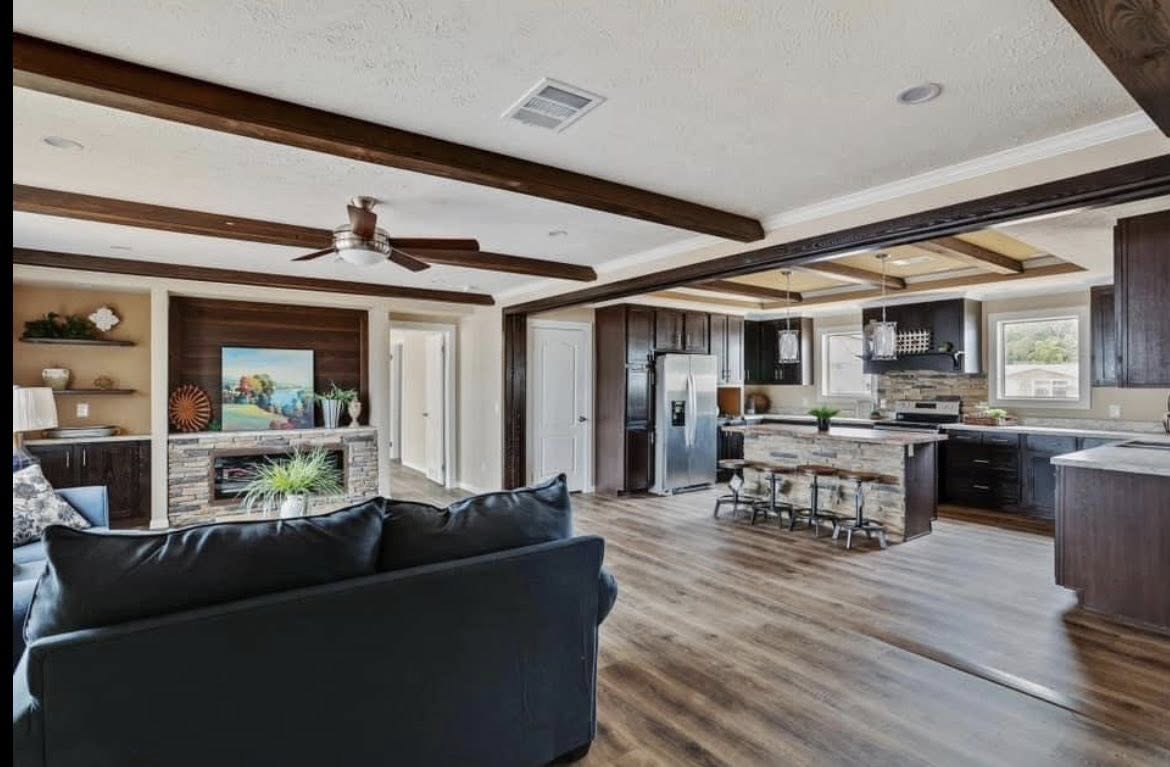 Spacious open-concept living room and kitchen with wooden beams, modern furnishings, and a cozy fireplace. The room feels warm and inviting.