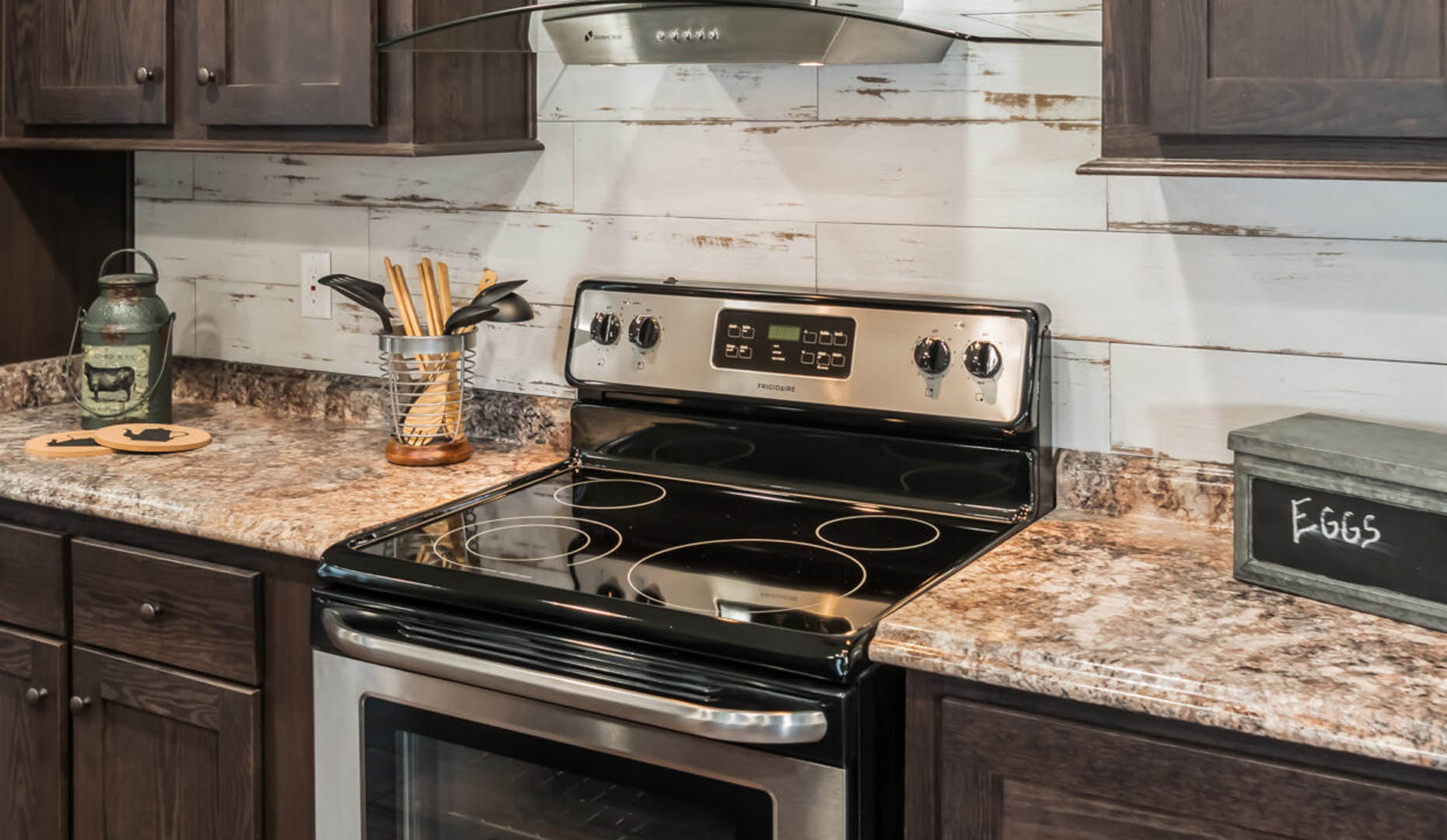 A cozy kitchen with dark wood cabinets, granite countertops, and a stainless steel stove. Rustic decor includes a woven utensil holder and a vintage-style container.