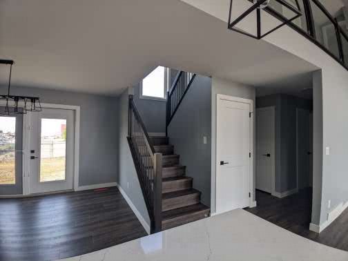 Modern, airy entrance with dark wood floors, a staircase leading up, a large window, and a glass door. Light gray walls create a minimalist feel.