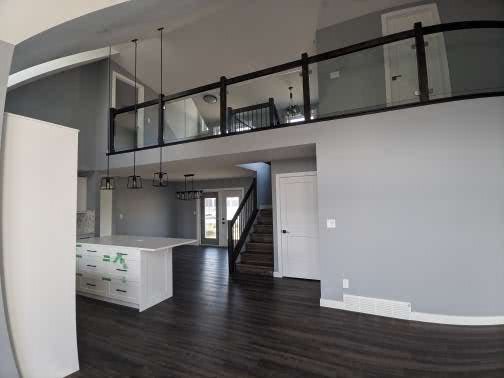 Modern, open-concept living area with high ceilings, dark wood floors, glass-railed mezzanine, minimalist kitchen island, and pendant lights creating a sleek, spacious ambiance.
