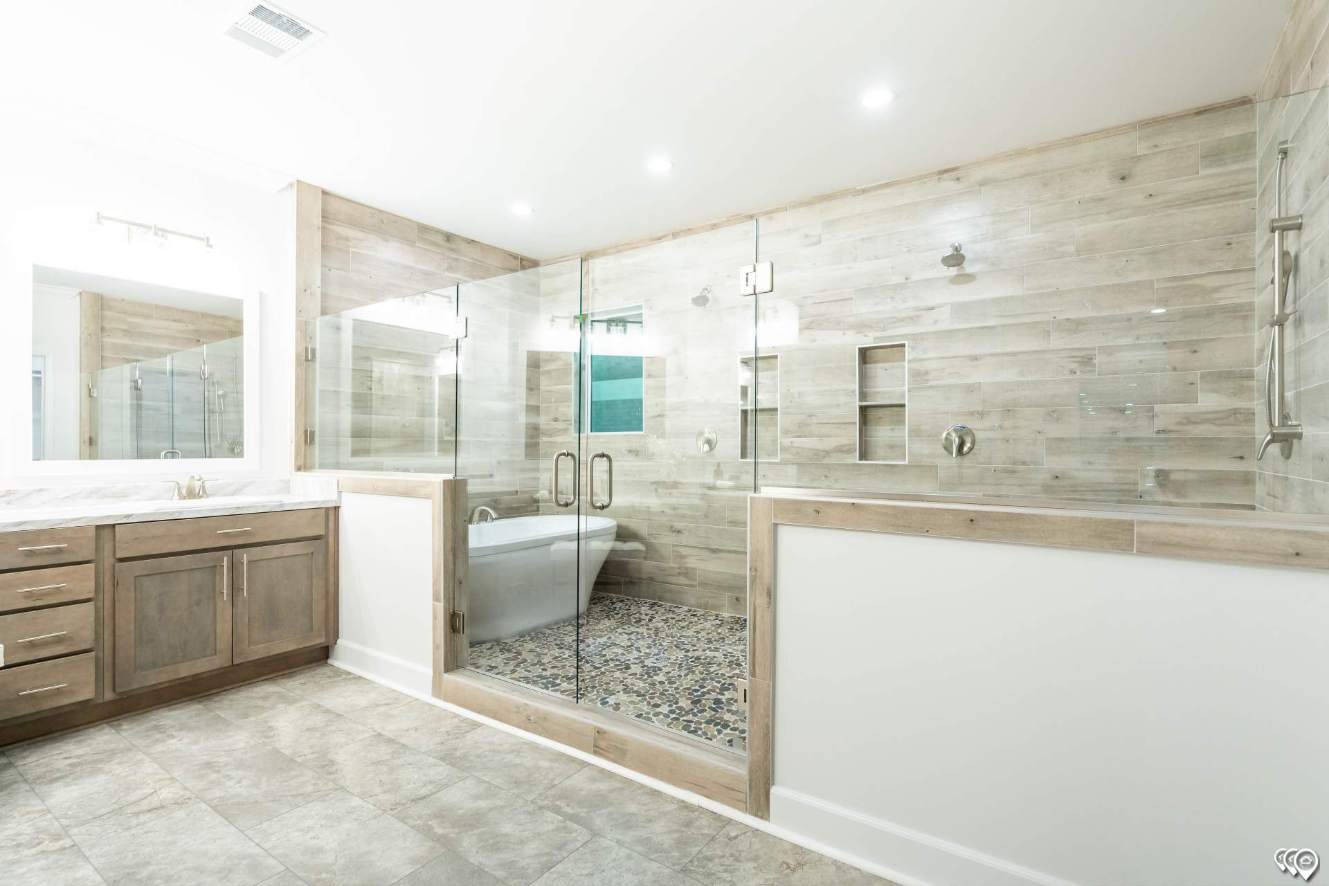 Spacious modern bathroom with wood-paneled walls, glass-enclosed shower, bathtub, large mirror, and vanity with several drawers, conveying elegance.