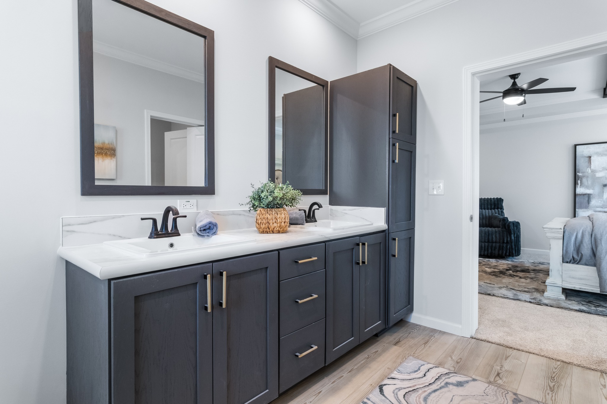 Sleek bathroom with dual sinks, dark wood cabinets, and large mirrors. A doorway reveals a cozy bedroom in neutral tones, exuding a calm and modern vibe.