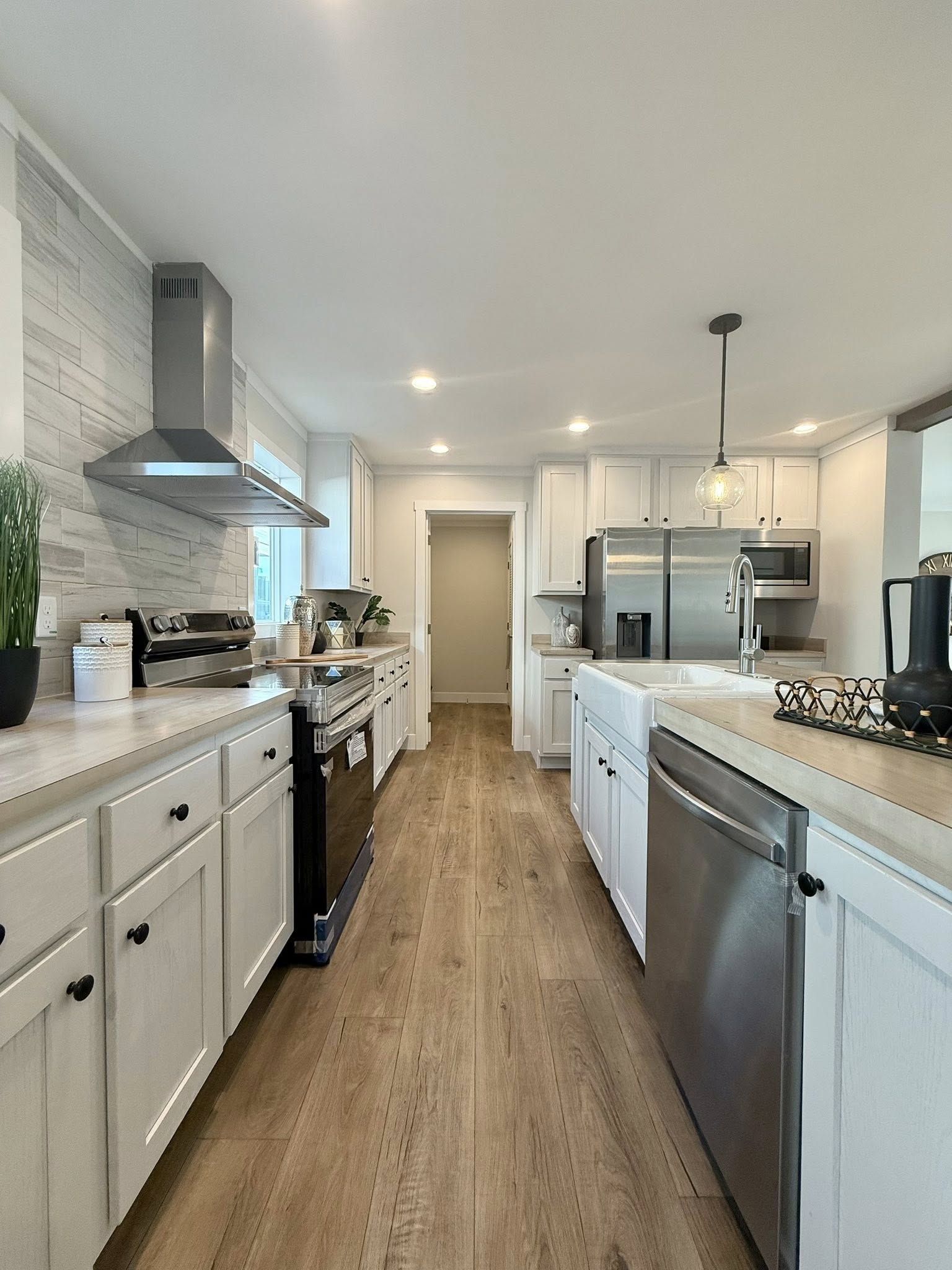 Spacious modern kitchen with white cabinets, stainless steel appliances, wood flooring, and pendant lighting. Clean, bright, and inviting atmosphere.