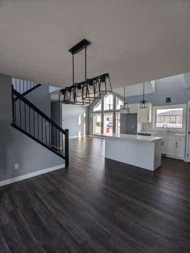 Modern open-plan kitchen and living space with dark wood floors, white walls, large windows, and a black metal staircase. Bright and airy atmosphere.