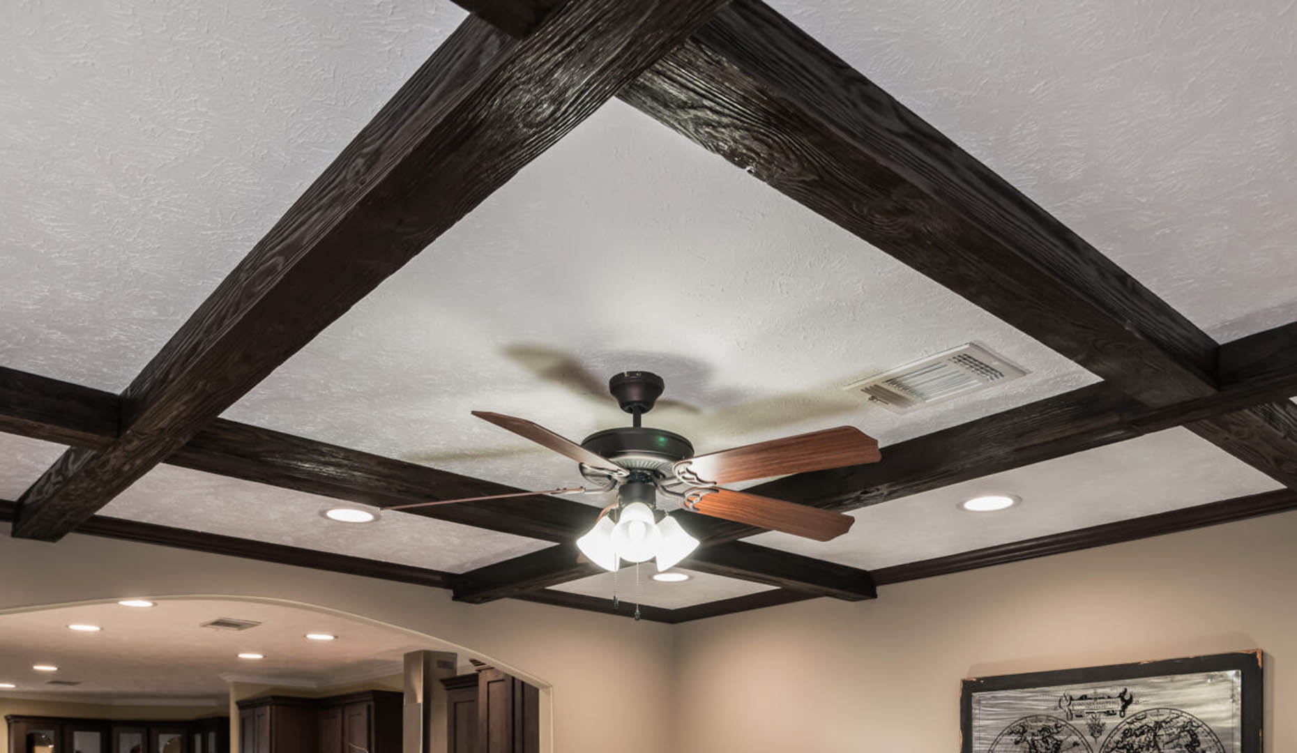 Ceiling with dark wooden beams in a grid pattern, featuring a central ceiling fan with light. The room feels cozy and modern, with recessed lighting.