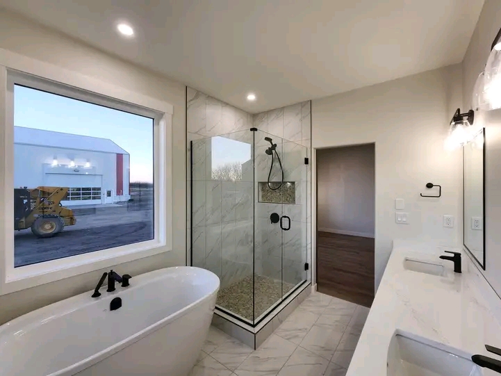Modern bathroom with a freestanding tub, glass-enclosed shower, and large window. Bright lighting and sleek design create a clean, tranquil atmosphere.