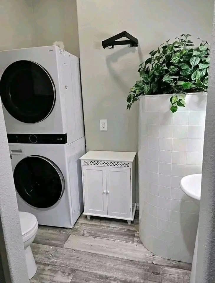Compact bathroom with stacked washer-dryer, small white cabinet, and curved tiled shower. Lush green plant adds a touch of nature.