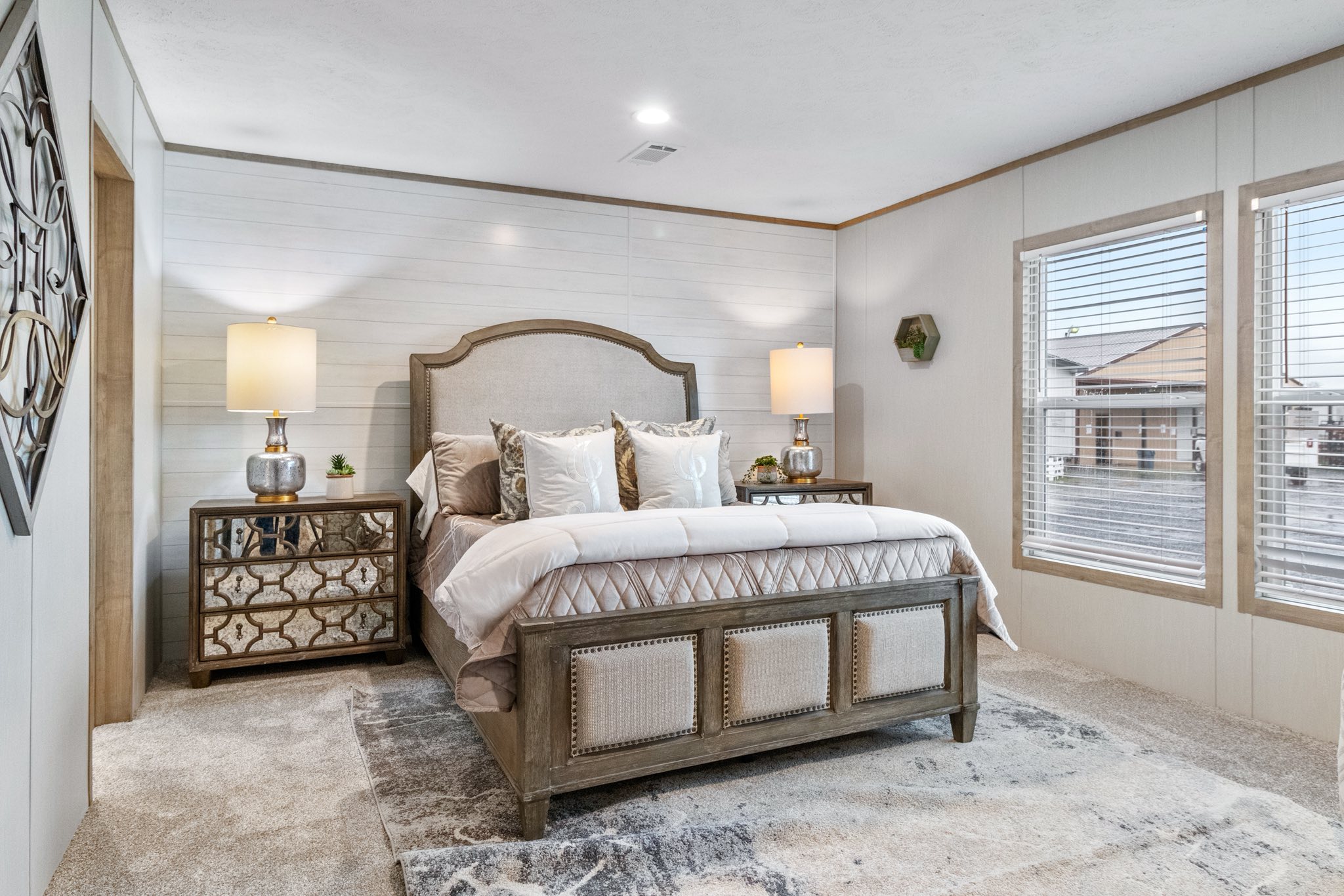 Luxury bedroom with an upholstered bed, elegant mirrored nightstands, and soft lighting from matching lamps. Large windows fill the space with natural light.