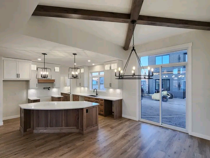 Modern kitchen with exposed beams, large island, and elegant chandeliers. Ample natural light from the glass sliding door to the outside.