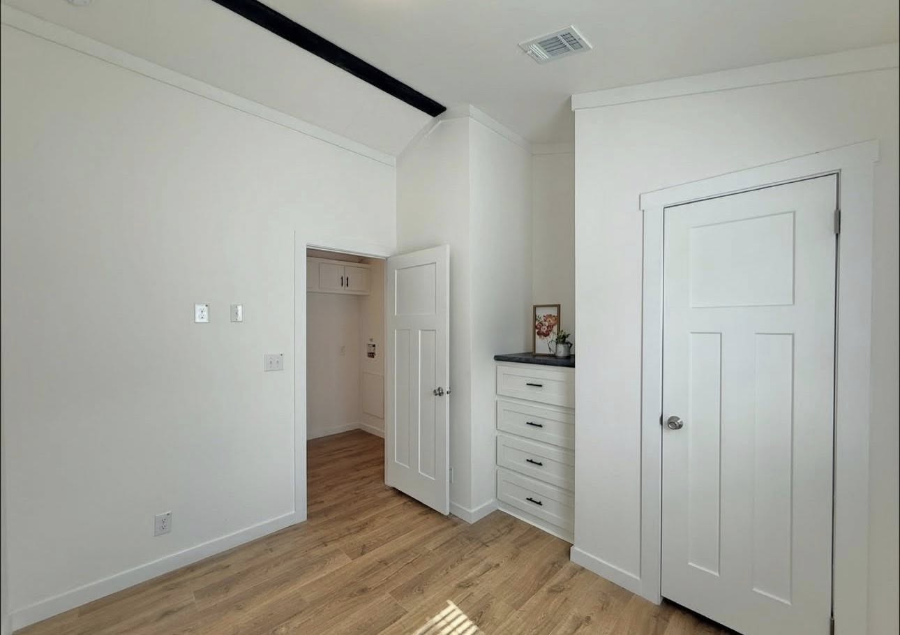 Bright, minimalist room with light wood flooring, white walls, and doors. Built-in closet and drawers to the right, creating a clean, modern vibe.