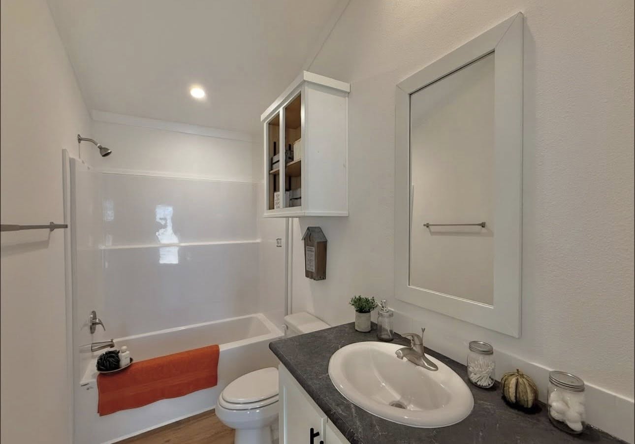 Modern bathroom featuring a white bathtub with an orange towel, black countertop with a sink, and decorative elements like a small plant and jars.