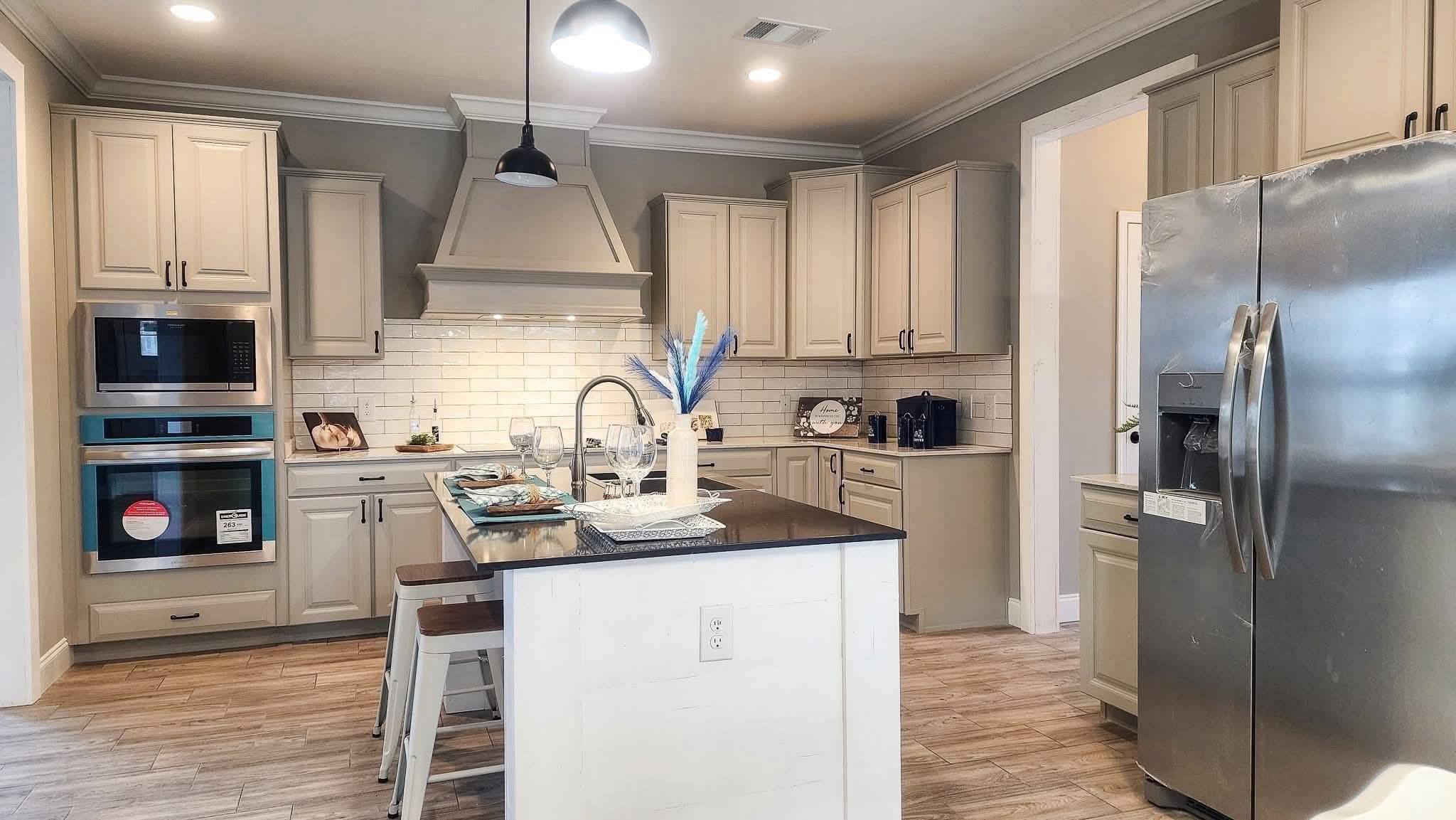 Spacious modern kitchen with beige cabinets, white subway tile backsplash, stainless steel appliances, and a central island with stools and decor.