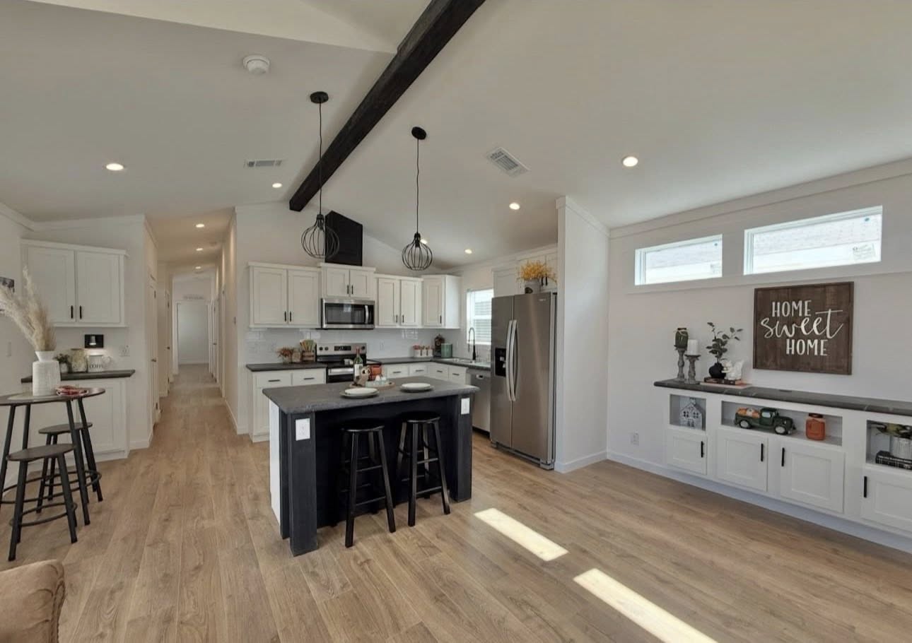 Bright, modern kitchen with white cabinets, stainless steel appliances, a dark island with stools, and a "Home Sweet Home" sign, creating a cozy ambiance.