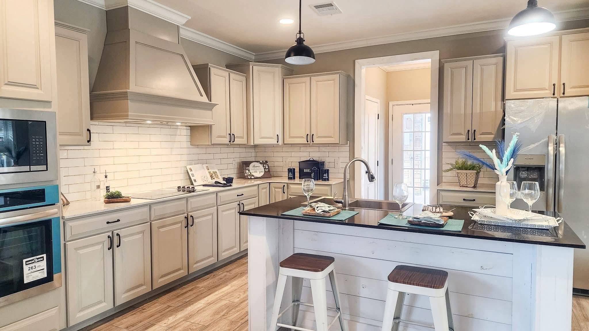 A modern kitchen with light wooden cabinets, stainless steel appliances, and a black countertop island with stools. Soft lighting creates a cozy feel.