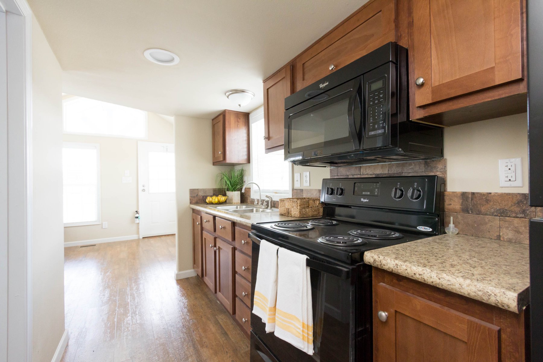 Compact kitchen with wooden cabinets, black appliances, and granite countertops. Bright window, hardwood floor, and a cozy, inviting atmosphere.