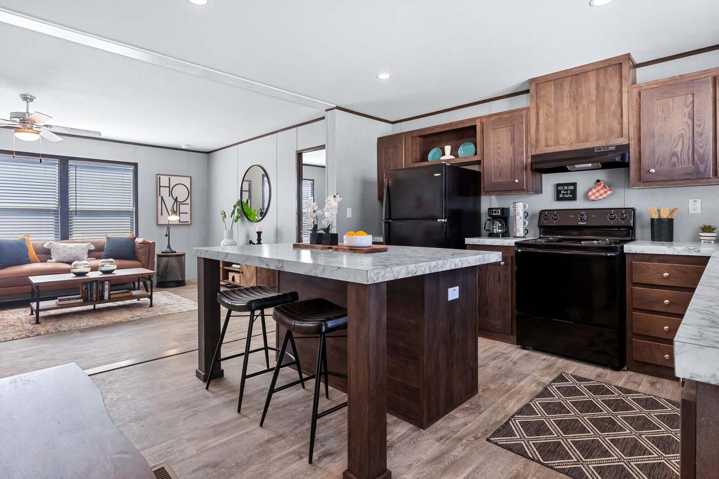 Modern open-plan kitchen and living room with dark wood cabinets, marble countertops, and a central island. Cozy seating area with a brown sofa.