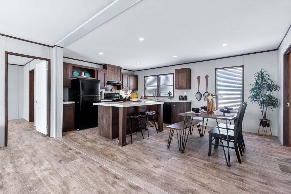 Modern kitchen and dining area with wooden flooring, dark cabinets, and black appliances. A dining table with chairs is set for a casual meal.