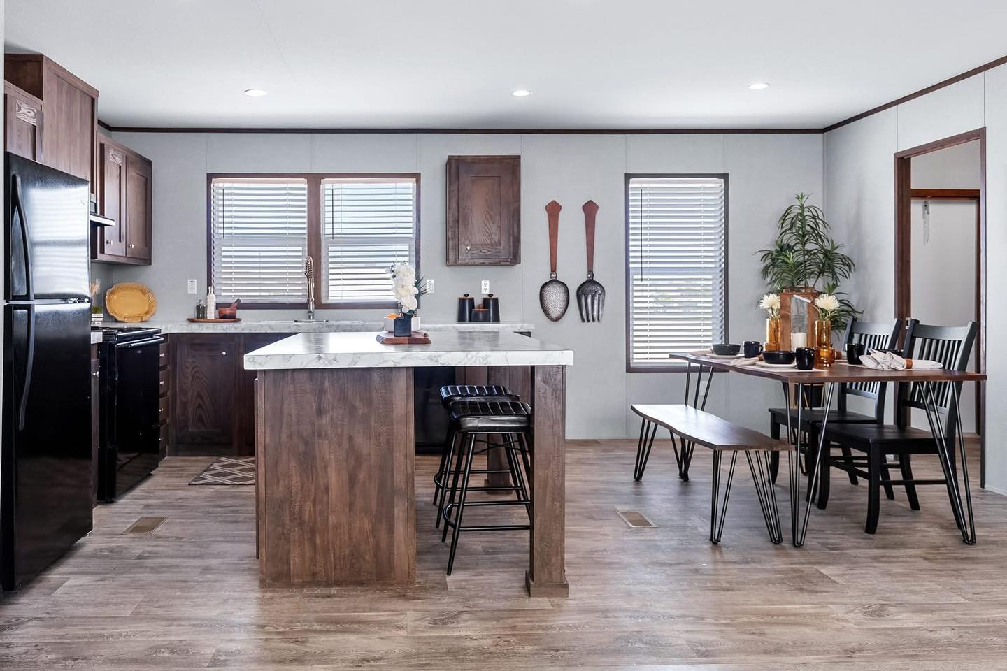 Modern kitchen with wood cabinets, island, and black bar stools. Adjacent dining area features a wooden table, black chairs, and a bench. Cozy and inviting.