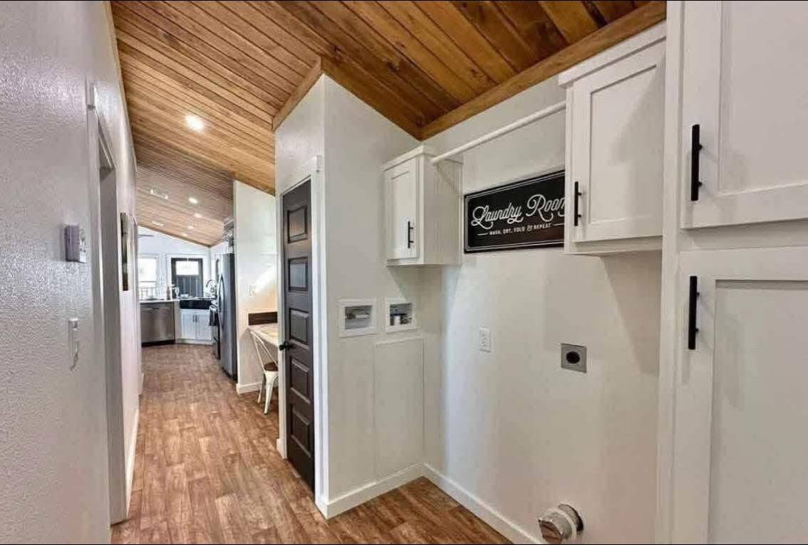 Narrow hallway with wood ceiling and floor, white walls, and cabinets. A "Laundry Room" sign is displayed. The space feels warm and inviting.