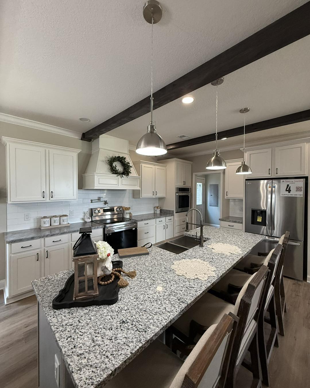 Modern kitchen featuring white cabinetry, stainless steel appliances, and granite countertops. Pendant lights hang over a large central island with bar stools.