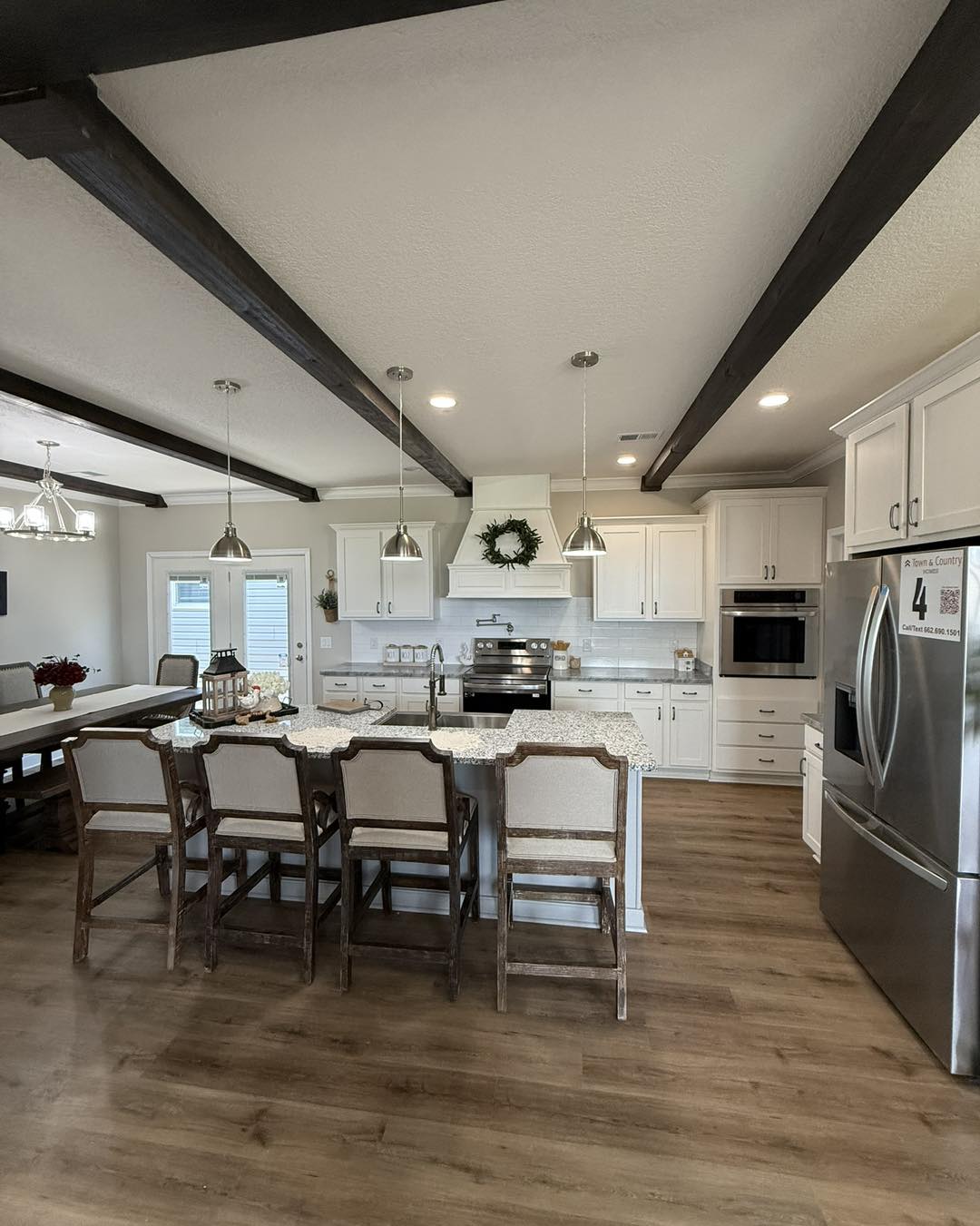 Modern kitchen with wooden beams, white cabinets, stainless steel appliances, and an island with barstools. Warm, inviting atmosphere.