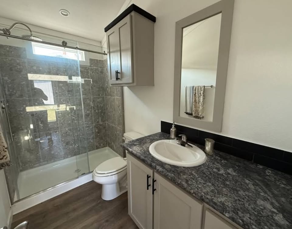 Modern bathroom with a glass-enclosed shower, gray marble tiles, a sleek vanity with a gray countertop, a mirror, and neutral-toned cabinets.