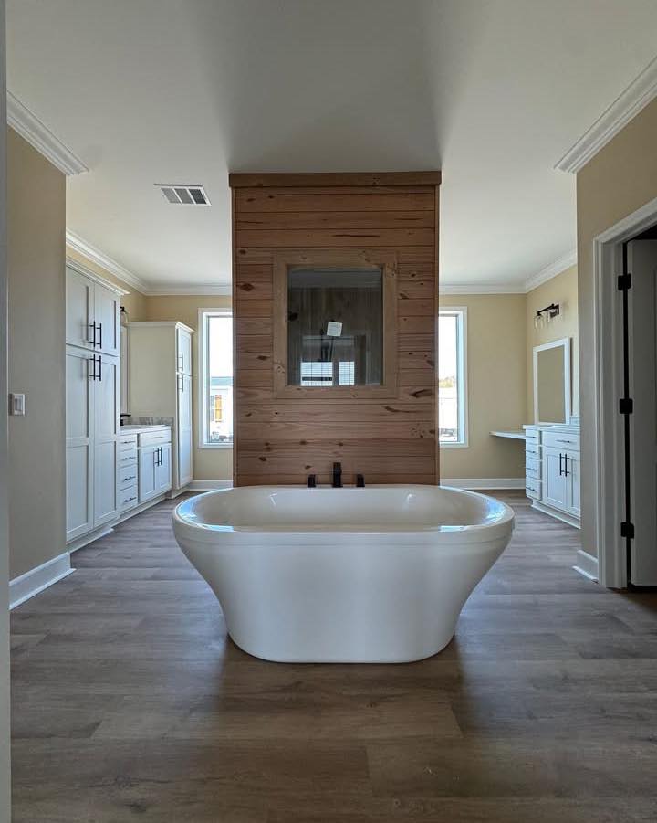 Elegant bathroom with a white freestanding tub centered on a wooden floor. Behind, a wooden accent wall divides the room. Bright and calming ambiance.