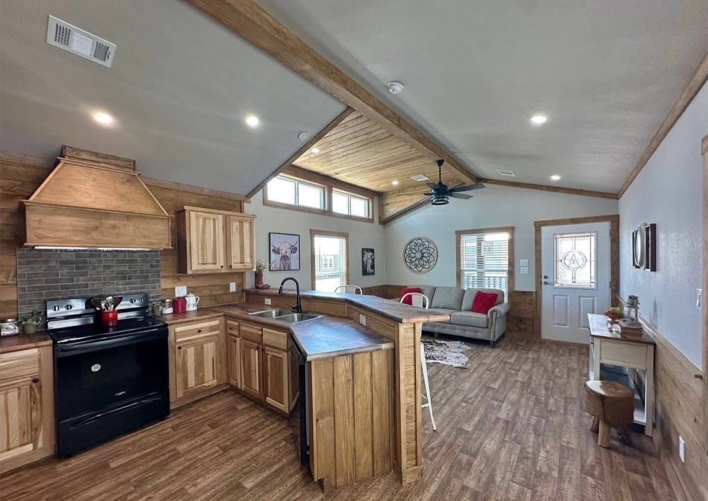 Rustic open-concept living area with wood accents, featuring a kitchen with natural cabinets, and a cozy living space with a gray sofa and decor.