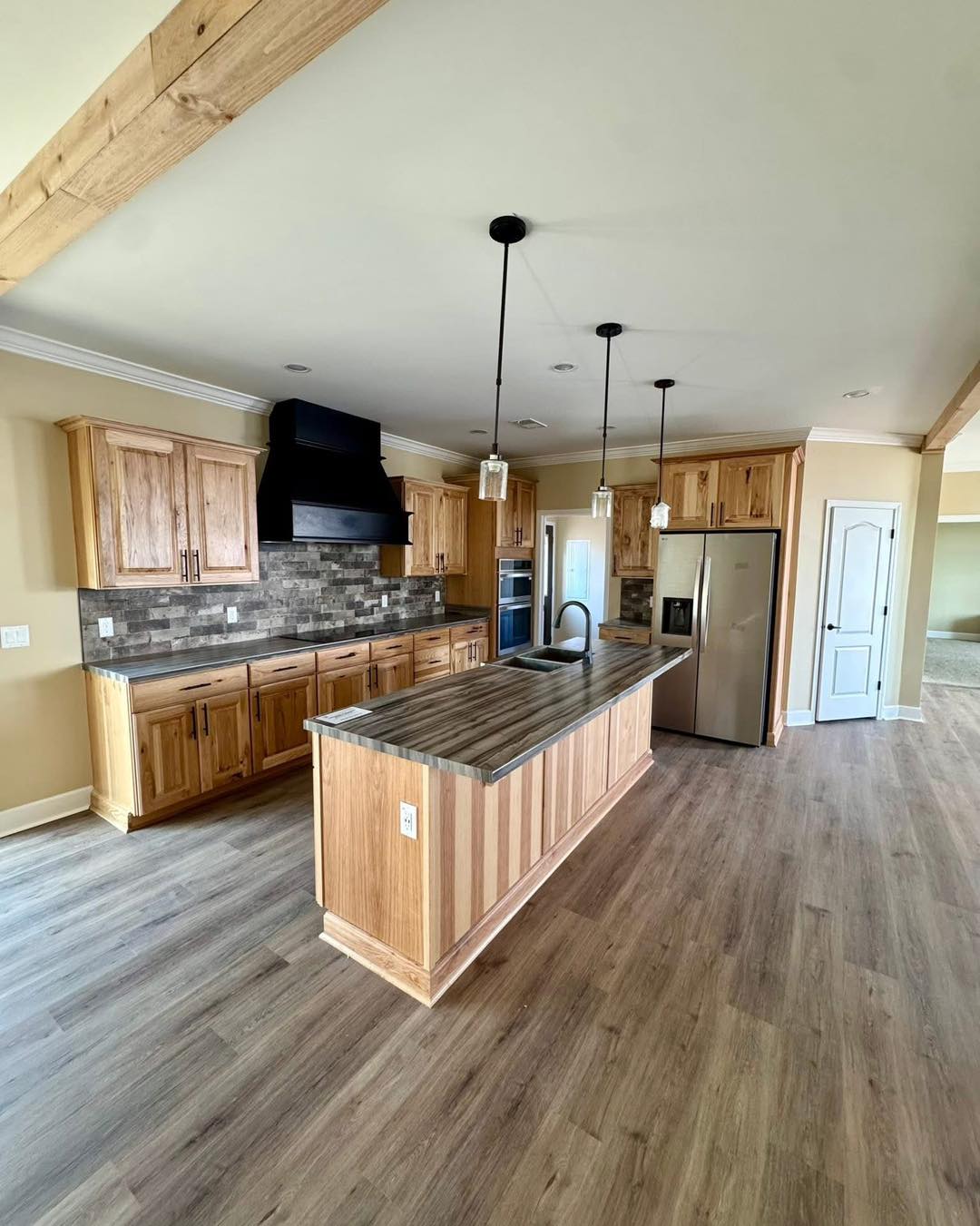 Spacious kitchen with wooden cabinets, stone backsplash, stainless steel appliances, and a long island with pendant lights. Modern and rustic ambiance.