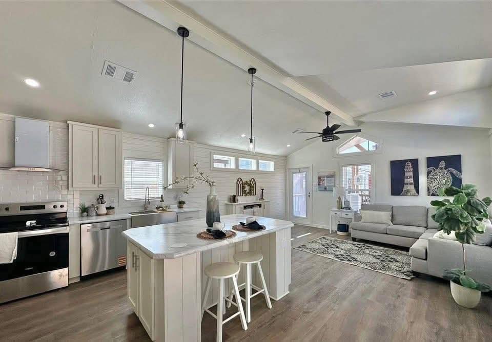 Modern open-concept kitchen and living area with white cabinetry, marble island, hanging lights, gray sofa, wooden flooring, and eye-catching artwork. Bright and welcoming ambiance.