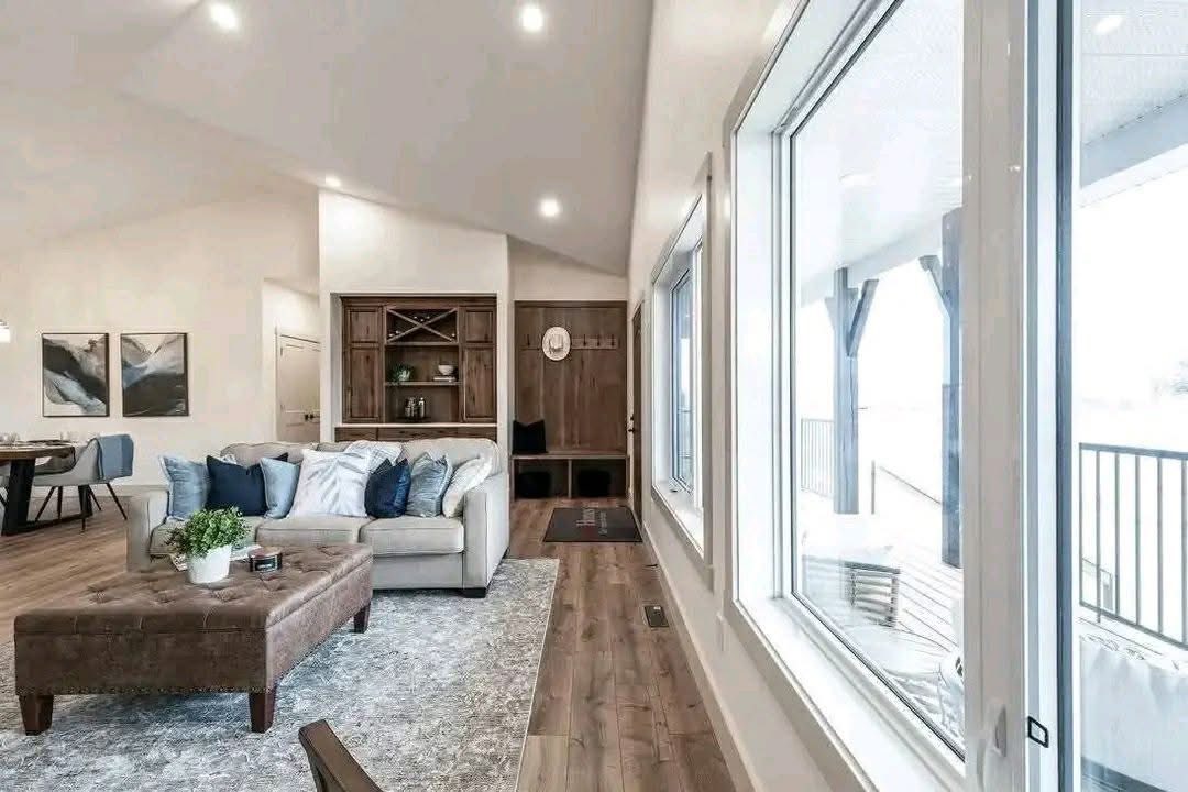 Spacious living room with a large window, light gray sofa adorned with blue cushions, wooden floors, and a cozy, elegant atmosphere.