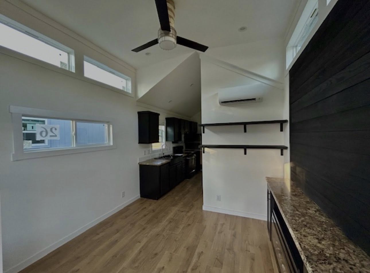 A modern kitchen with high ceilings, dark cabinets, marble countertops, and wooden floors. Natural light streams through high windows, creating an airy feel.