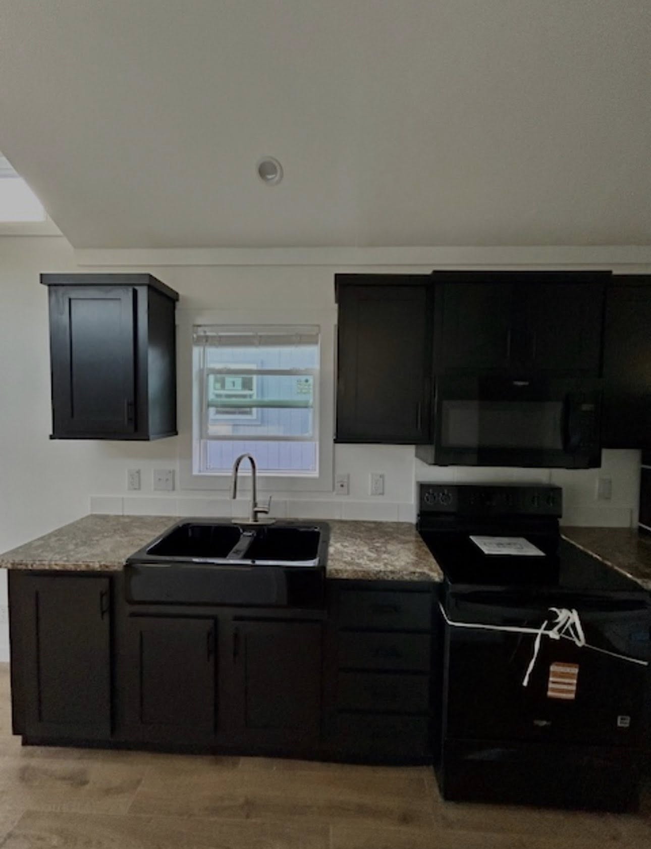 Modern kitchen with dark cabinets, a granite countertop, black sink, and appliances. A window above the sink lets in natural light, creating a sleek, clean look.