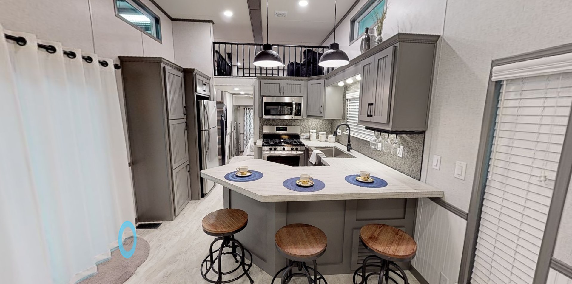 Modern kitchen with gray cabinets, stainless steel appliances, and a central island. Three wooden stools and blue placemats add warmth and color. Bright, open space.