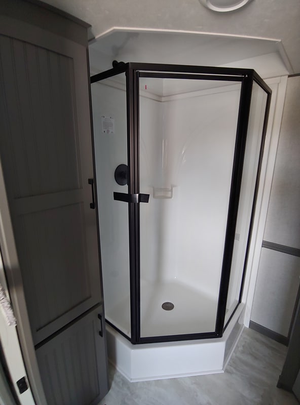 A modern, compact shower enclosure with black frame and clear glass in a white bathroom. Adjacent is a gray cabinet with sleek handles. Clean, minimalist vibe.