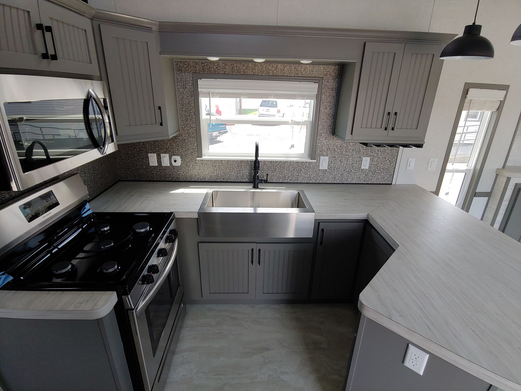 Modern kitchen with gray cabinets and stainless steel appliances, including a stove and deep sink. Bright window view adds natural light.