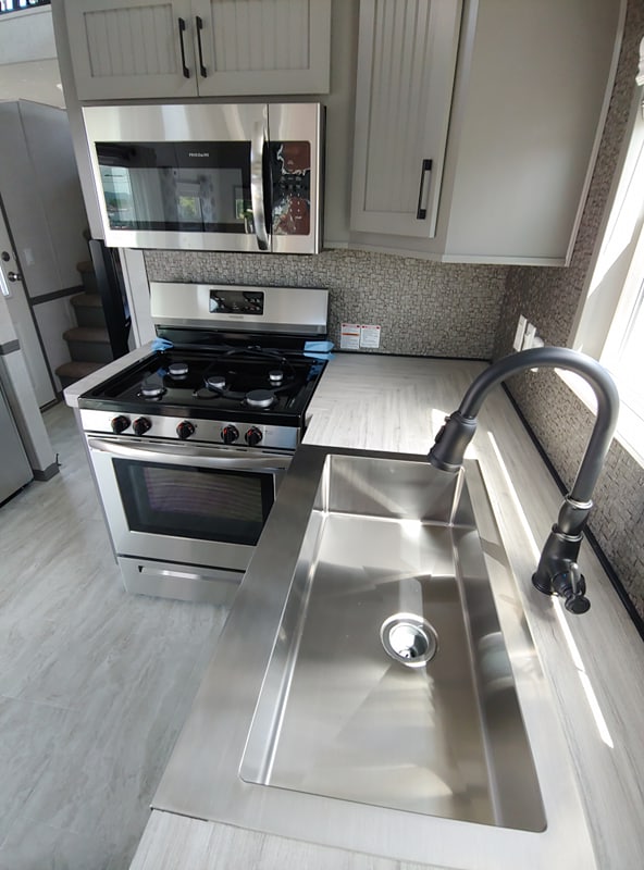 Modern kitchen with a stainless steel oven and matching microwave, large sink with a curved faucet, set against light cabinets and textured backsplash.