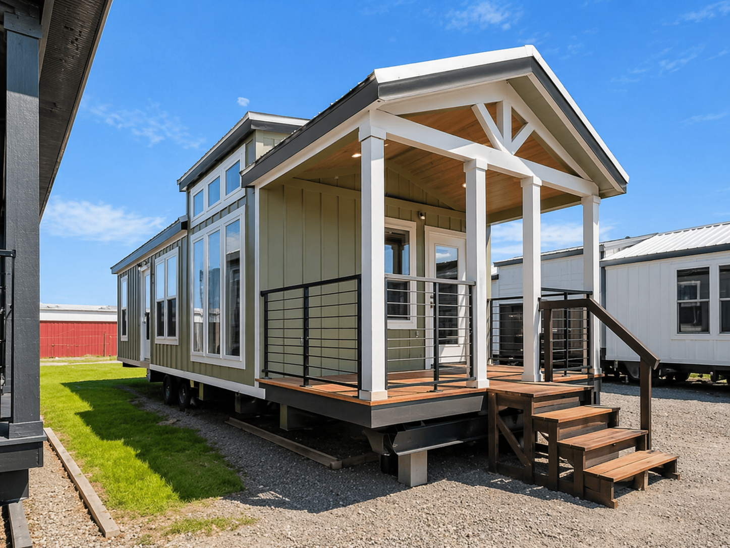 Stylish tiny house with a modern porch, white columns, and large windows under a clear blue sky. The exterior is green with a cozy, welcoming feel.