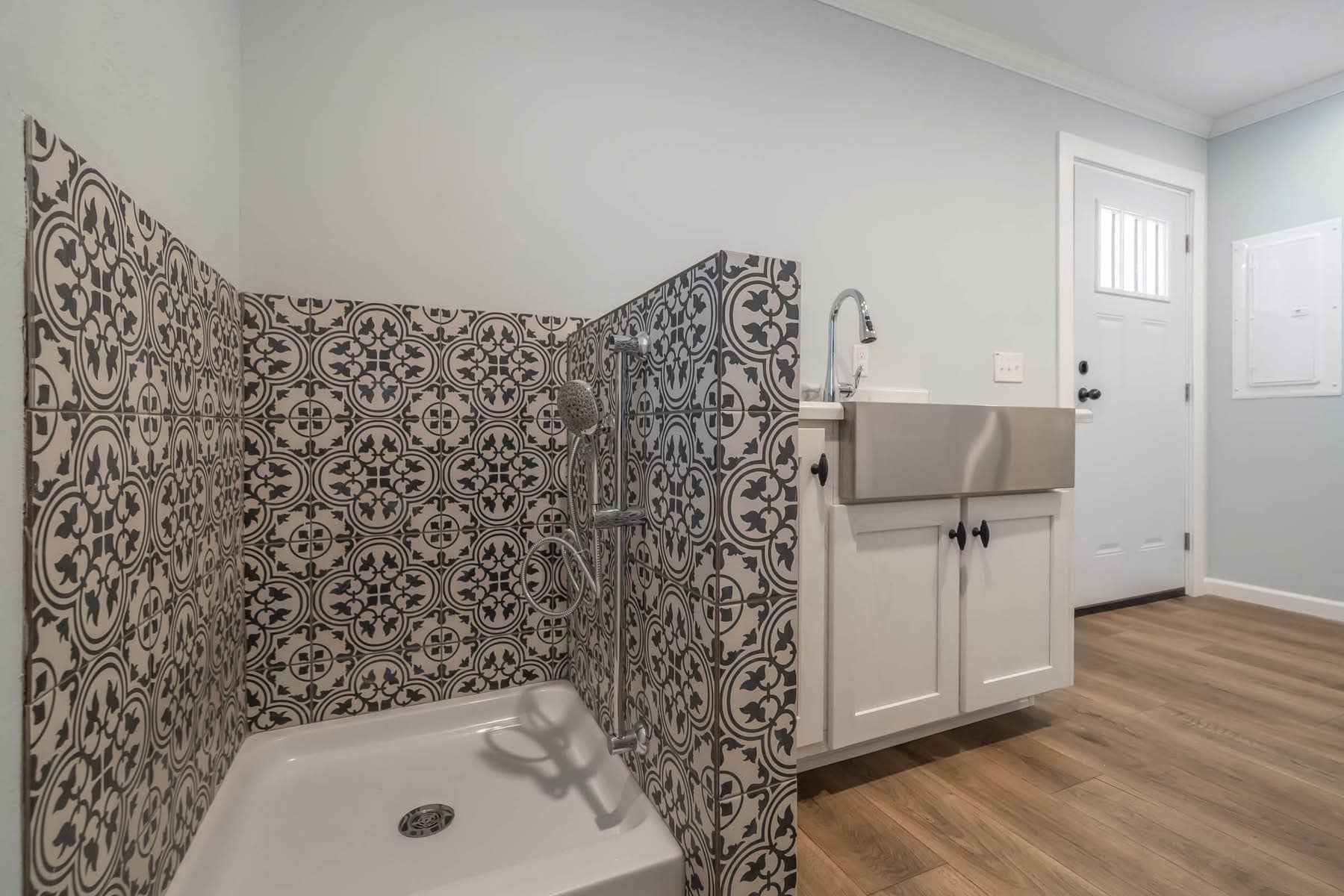 The image shows a utility room with patterned tiles around a pet washing station, a stainless steel sink, and white cabinets, creating a clean, modern feel.