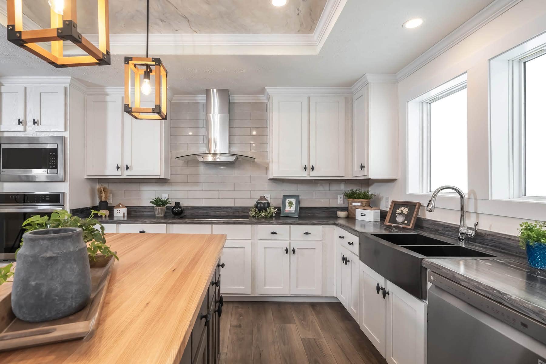 Modern kitchen with white cabinets, gray countertops, and stainless steel appliances. Wooden island with a potted plant adds a warm touch.