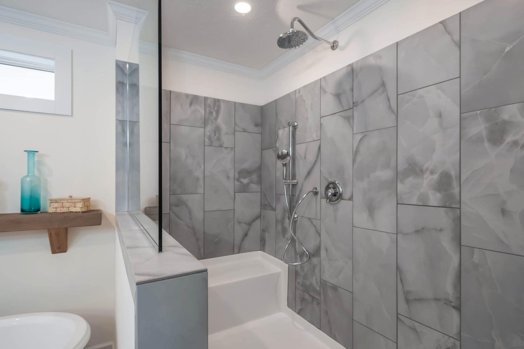 Modern bathroom with sleek gray marble tiles, a walk-in shower with a chrome showerhead, and a small bench. A glass partition adds elegance.