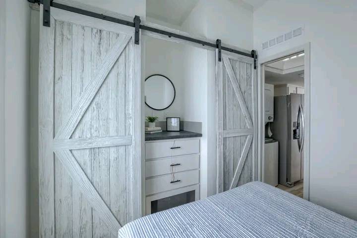 Bedroom with rustic white sliding barn doors leading to a closet with drawers. A round mirror hangs above the dresser, creating a cozy ambiance.