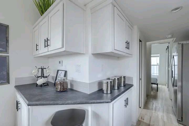 Modern kitchen corner with white cabinetry and sleek black handles. A gray countertop holds jars and a small coffee machine. Bright, airy feel.
