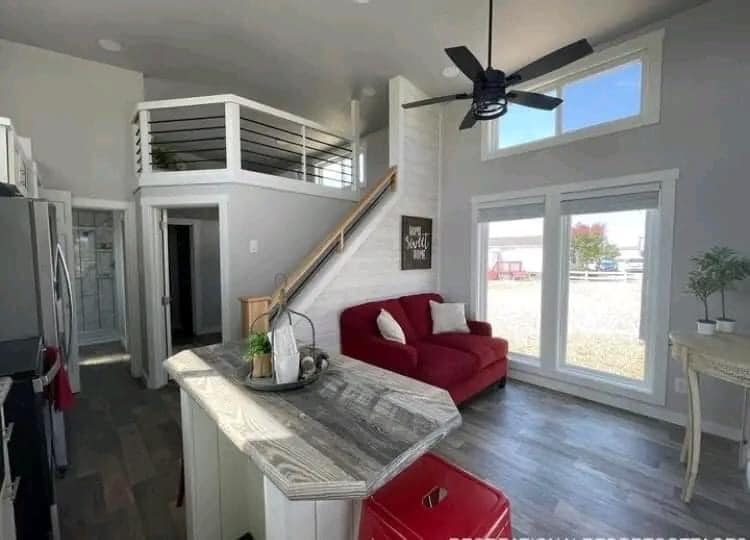 Modern tiny house interior with open loft. Red sofa and decor against white walls create a cozy feel. Large windows and high ceilings add brightness.