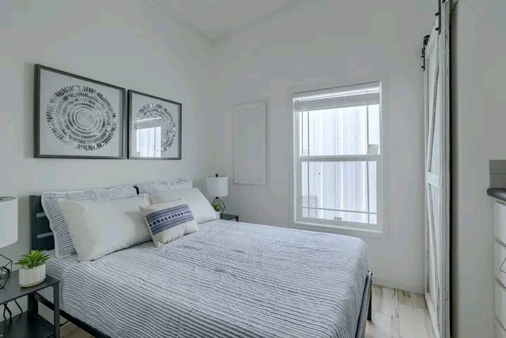 A cozy, minimalist bedroom with a neatly made bed featuring striped bedding. Two abstract prints hang above the bed, next to a window with soft light.